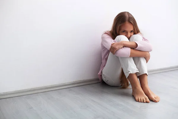 Jonge bezorgd of verdrietig meisje zittend op de vloer door de muur — Stockfoto