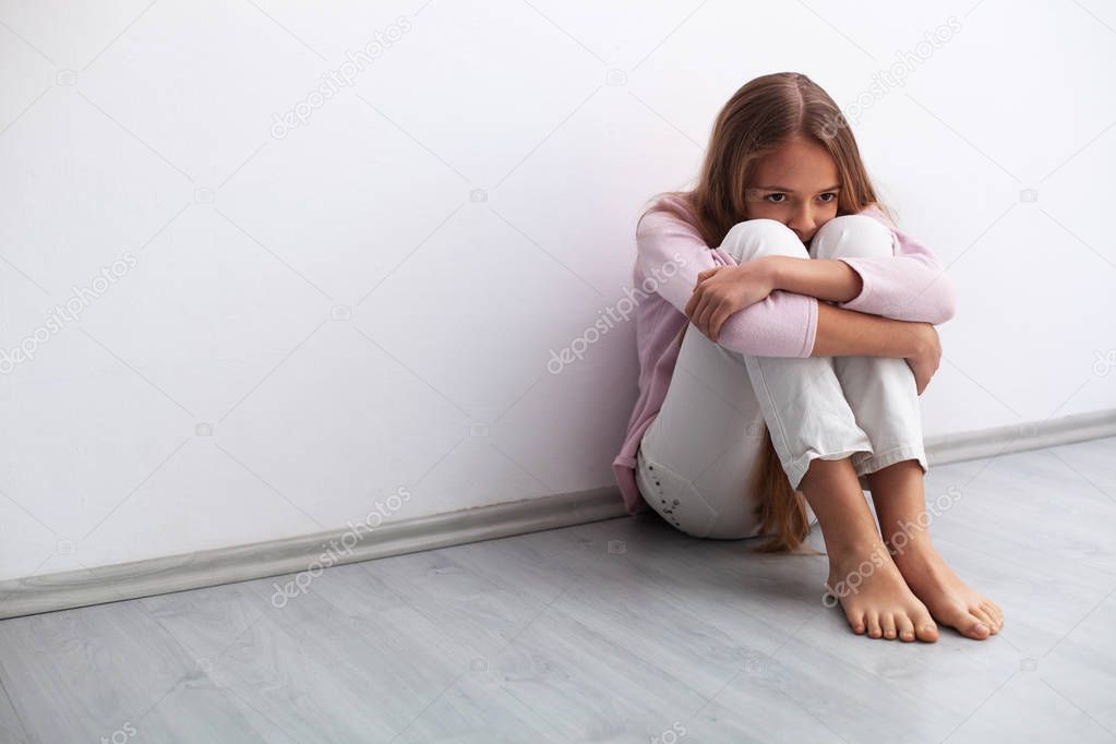 Young worried or sad girl sitting on the floor by the wall