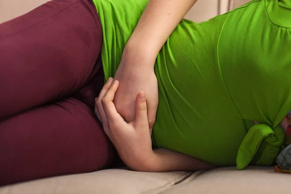 Karın ağrısı olan genç bir kız kanepede yatıyor. Gövdesine yakın. — Stok fotoğraf