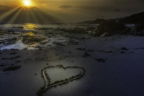 Romantic view of heart shape in sand with sunset background