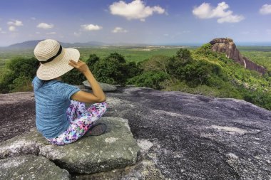 A woman in a hat sitting and looking into the surrounding landscape from a large stone Baginda /Belitung-Indonesia/