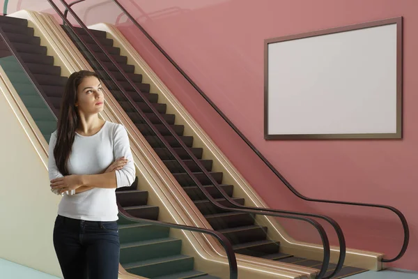 在现代粉红色地铁站站在一个体贴的年轻欧洲妇女与自动扶梯和空海报 商业概念 — 图库照片