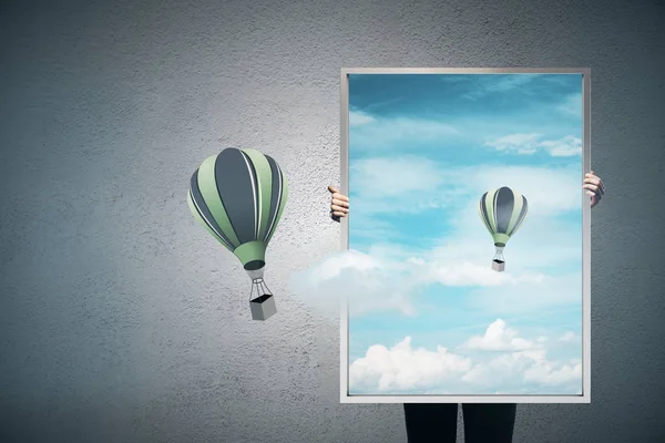 think outside the box concept with person holding picture frame with sky and flying balloons inside at concrete wall background