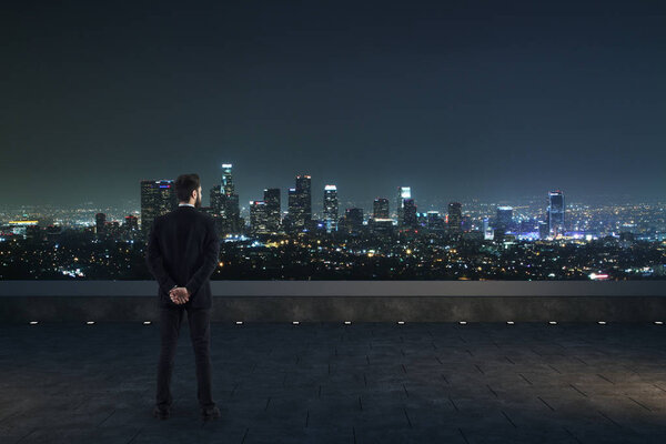 Back view of businessman on rooftop looking into the distance on night city background. Future concep