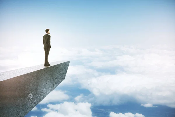 青空に雲の上のコンクリートの崖の上で遠くを見つめるビジネスマン — ストック写真