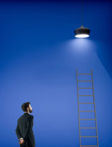 はしご ランプ コピー スペースと青色の背景の上に立って思いやりのある青年実業家の側面図です 成功とプロモーションの概念 — ストック写真