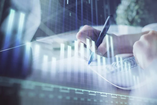 Financial forex graph displayed on hands taking notes background. Concept of research. Multi exposure