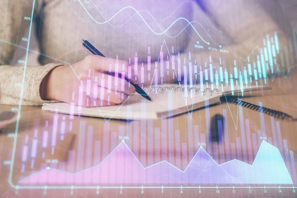 Mãos escrevendo informações sobre o mercado de ações no bloco de notas. hologramas gráfico Forex na frente. Conceito de pesquisa. Exposição múltipla — Fotografia de Stock