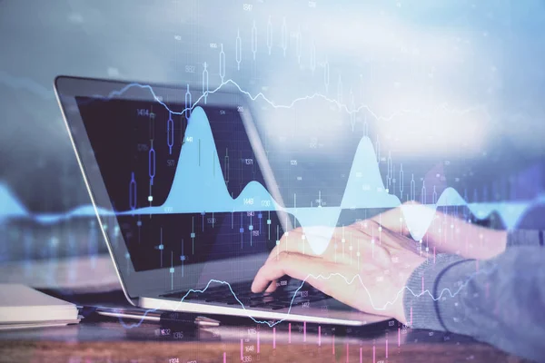 Double exposure of businessmans hands with laptop and stock market graph background. Concept of research and trading.