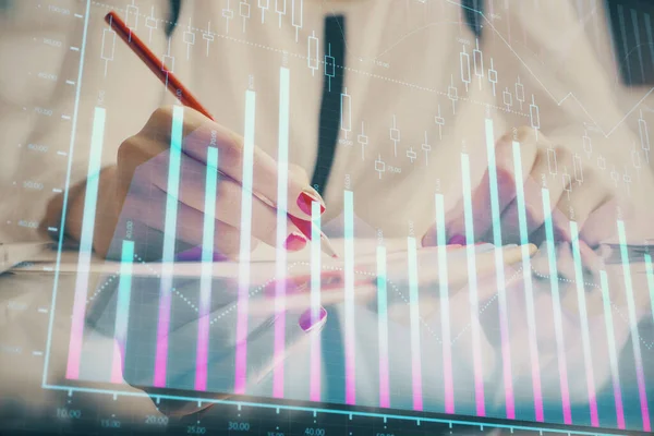 Una mujer escribe información sobre el mercado de valores en bloc de notas. Hologramas gráfico de divisas en frente. Concepto de investigación . —  Fotos de Stock