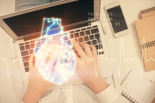 Double exposition des mains de la femme travaillant sur l'ordinateur et le dessin de l'hologramme cardiaque. Vue du dessus. Concept de science médicale. — Photo