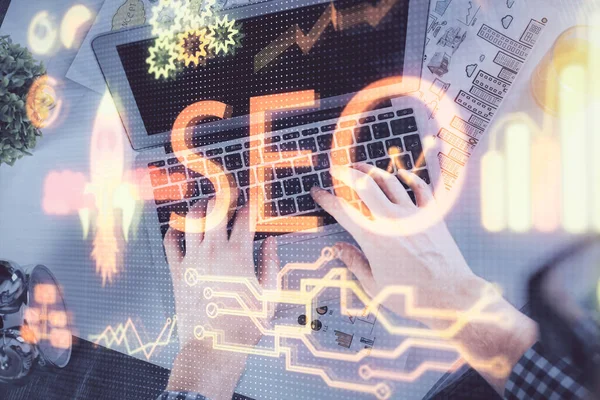 Multi exposure of mans hands typing over computer keyboard and SEO hologram drawing. Top view. Search optimization concept. — Stock Photo, Image