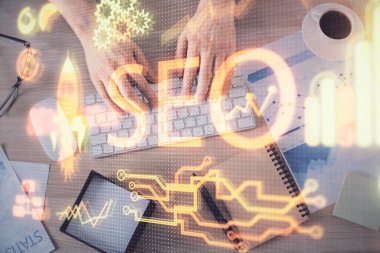 Bilgisayar klavyesinin ve SEO hologram çiziminin üzerine yazı yazan bir adamın eline çok kez maruz kalmış. Üst Manzara. Arama optimizasyon kavramı.