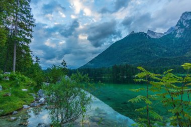 Açık bir dağ gölü. Arkasında kara bulutlar ve yüksek dağlar var.