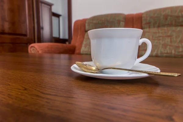 一个白色的杯子 上面有一个茶托和一个勺子 站在沙发附近的木桌上 — 图库照片