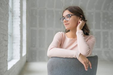 Genç Sevimli seksi sevimli kız elbise ve gevşek saç gri bir koltukta oturan büyük pencereler ile bir beyaz odada bardaklarda gebe