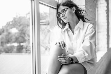 Genç Sevimli seksi sevimli kız elbise ve gevşek saç gri bir koltukta oturan büyük pencereler ile bir beyaz odada bardaklarda gebe