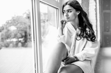 Genç Sevimli seksi sevimli kız elbise ve gevşek saç gri bir koltukta oturan büyük pencereler ile bir beyaz odada bardaklarda gebe