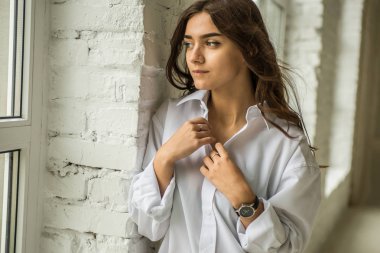 Genç Sevimli seksi sevimli kız elbise ve gevşek saç gri bir koltukta oturan büyük pencereler ile bir beyaz odada bardaklarda gebe