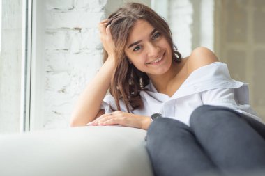 Genç Sevimli seksi sevimli Gözlüklü kız çıplak sarıl bağsız kıl ile büyük bir pencere yakınında ile beyaz bir erkek ceket beyaz kanepe oturur gebe