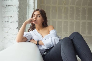 Genç Sevimli seksi sevimli Gözlüklü kız çıplak sarıl bağsız kıl ile büyük bir pencere yakınında ile beyaz bir erkek ceket beyaz kanepe oturur gebe