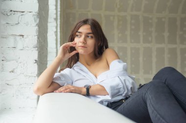 Genç Sevimli seksi sevimli Gözlüklü kız çıplak sarıl bağsız kıl ile büyük bir pencere yakınında ile beyaz bir erkek ceket beyaz kanepe oturur gebe