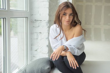 Genç Sevimli seksi sevimli Gözlüklü kız çıplak sarıl bağsız kıl ile büyük bir pencere yakınında ile beyaz bir erkek ceket beyaz kanepe oturur gebe