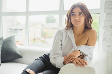 Genç Sevimli seksi sevimli Gözlüklü kız çıplak sarıl bağsız kıl ile büyük bir pencere yakınında ile beyaz bir erkek ceket beyaz kanepe oturur gebe