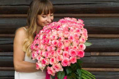 Genç güzel hoş tutan gülümseyerek bir ışık ve uzun saçlı kız ile büyük bir ahşap bir duvarın yanında ayakta beyaz ve kırmızı gül buketi