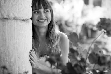 Genç güzel uzun saçlı kız nezaketle taş duvar ve kırmızı çiçekler gülümseyen bir ışık ile 