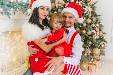 bir adamın annesi ve babasının kucağına bir ağaç ve bir festival elbiseli şömine yakın oturan küçük bir kızı Genç Sevimli gülümseyen aile