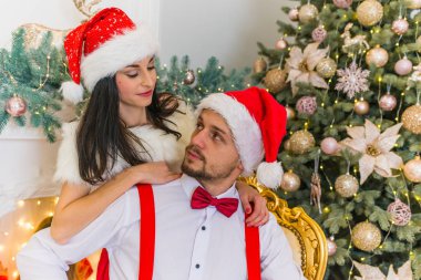 sevimli sevimli baştan çıkarıcı kız ve kırmızı yılbaşı şapka şenlikli bir Noel ağacı, şenlikli bir fotoğraf yakınındaki bir chrisble oturan küçük bir sakallı bir adam