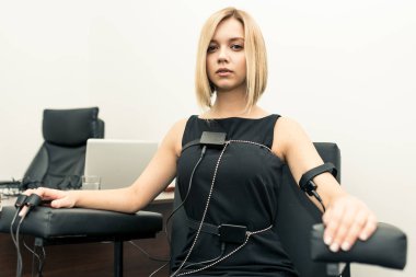 Hafif saçlı polygraphs masanın üstüne giyinmiş olan siyah bir elbise giymiş bir kadın vardır yalan makinesi, dizüstü bilgisayar ve aygıtları