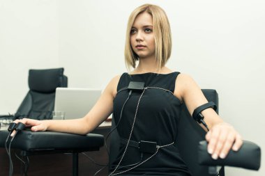 Hafif saçlı polygraphs masanın üstüne giyinmiş olan siyah bir elbise giymiş bir kadın vardır yalan makinesi, dizüstü bilgisayar ve aygıtları