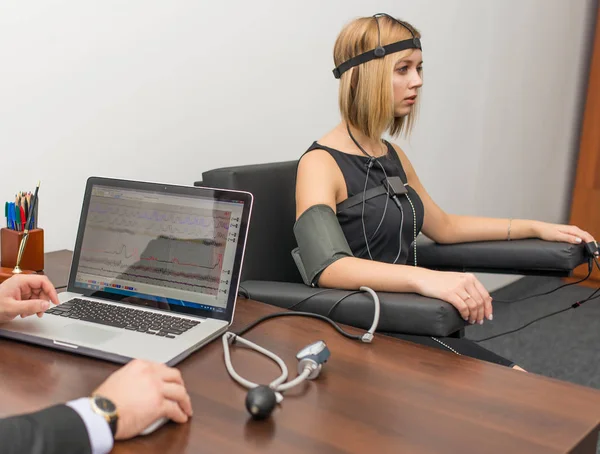 Hafif saçlı polygraphs masanın üstüne giyinmiş olan siyah bir elbise giymiş bir kadın vardır yalan makinesi, dizüstü bilgisayar ve aygıtları