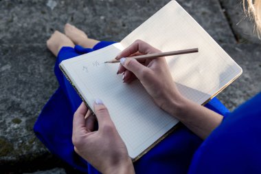 basamaklarında oturan ve bir kalem bir defterde yazılı mavi elbiseli kız