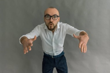 Genç güzel, şık adam gözlüklü gri bir arka planda, duygusal karanlık pantolon ve gösterileri hareketleri elleri ile parlak gömlekli sakallı