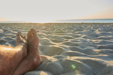 Erkeklerin ayaklarında sunrise, güneş ışınlarının yakınındaki plajda 