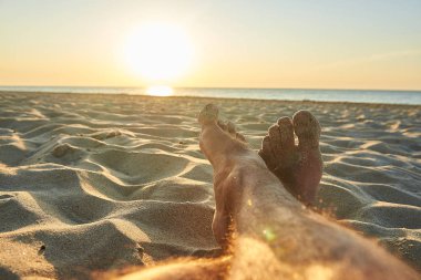 Erkeklerin ayaklarında sunrise, güneş ışınlarının yakınındaki plajda 