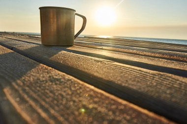 Doğu güneşin deniz kıyısında ahşap plakalar üzerinde metal bir kupa