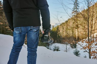 Mavi jeans ve onu elinde tutar bir kamera ile dağlarda bir kış ceket bir adam