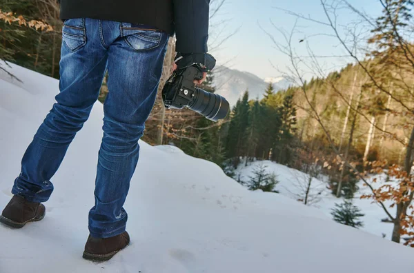 a man in blue jeans and a winter jacket in the mountains with a camera that holds him in his hands