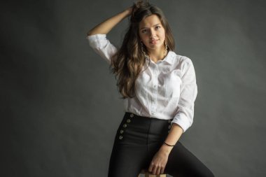 genç güzel büyüleyici baştan çıkarıcı kız bağsız kıl ile beyaz bir gömlek gri bir arka plan bir tahta sandalyede yanında ayakta