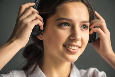 kulaklık müzik dinler gri bir arka plan üzerinde beyaz bir gömlek giymiş güzel bir gülümseme ile ahlaksız sarı saçlı güzel bir genç kızla portresi