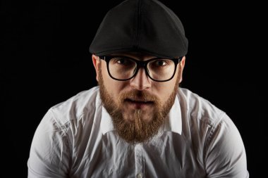 Gözlük sakallı genç bir adam ve bıyıklı bir siyah şapka ve beyaz bir gömlek, bir karanlık studio arka plan portresi
