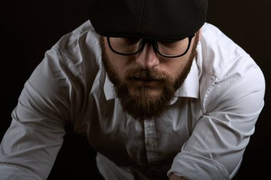 Ellerinde bir karanlık studio arka plan bükülmüş mücadele ve bıyıklı bir siyah şapka ve beyaz bir gömlek gebe bardak genç yakışıklı adam