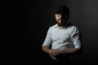 Gözlük sakallı genç bir adam ve bıyıklı bir siyah şapka ve beyaz bir gömlek, bir karanlık studio arka plan portresi