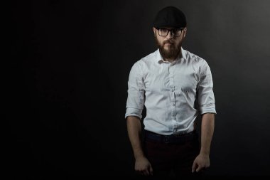 Gözlük sakallı genç bir adam ve bıyıklı bir siyah şapka ve beyaz bir gömlek, bir karanlık studio arka plan portresi