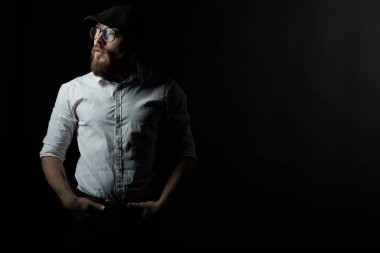 Gözlük sakallı genç bir adam ve bıyıklı bir siyah şapka ve beyaz bir gömlek, bir karanlık studio arka plan portresi