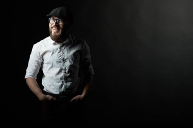 Gözlük sakallı genç bir adam ve bıyıklı bir siyah şapka ve beyaz bir gömlek, bir karanlık studio arka plan portresi